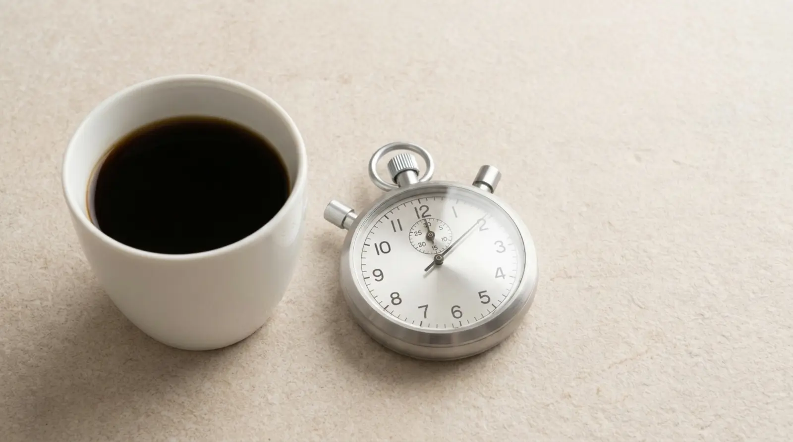 A white cup of black coffee beside a simple analogue stopwatch on a pale surface in soft even daylight, both objects plain and unbranded