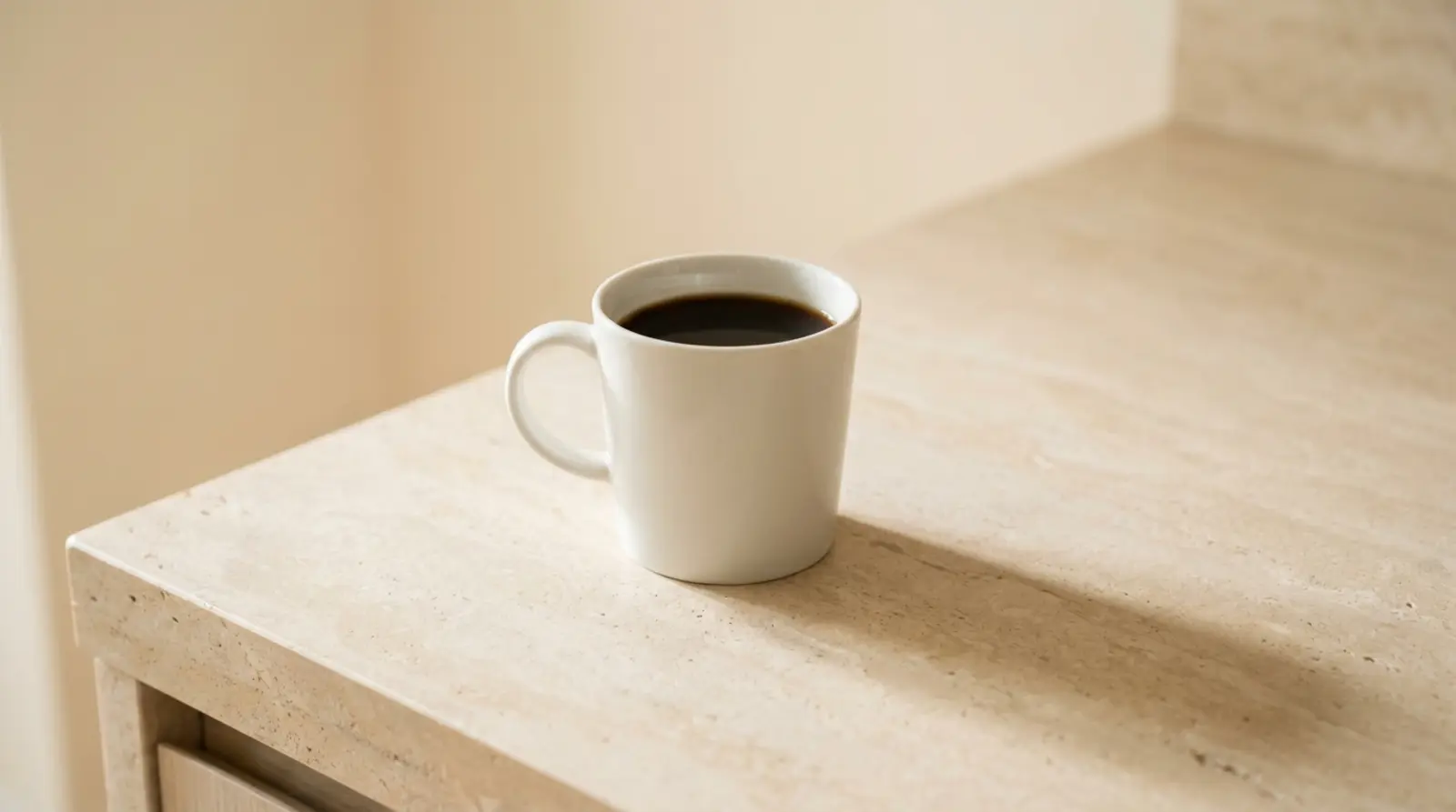 A plain white cup of black coffee on a pale stone surface in soft even daylight, quiet and clinical with generous negative space