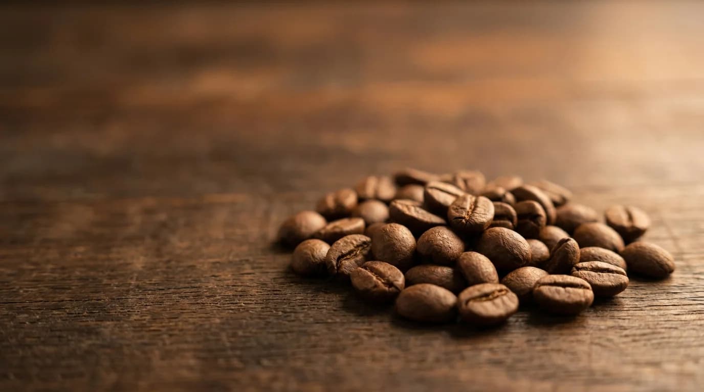 A close-up pile of small round robusta coffee beans on a dark wooden surface, slightly smaller and rounder than arabica beans, warm side-lighting showing texture, minimalist composition