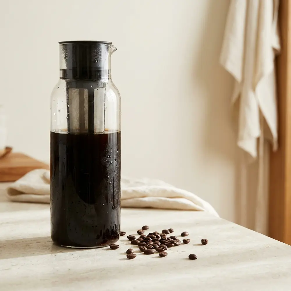 A tall glass cold brew carafe of dark coffee with a mesh filter column, condensation on the glass